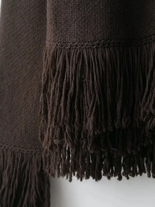 Detailed macro view of dark brown knitted fabric with premium fringe trim and texture