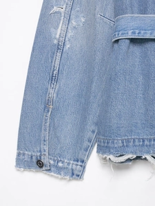Détail d'une veste en jean bleu clair avec bouton en métal, trous et bords effilochés
