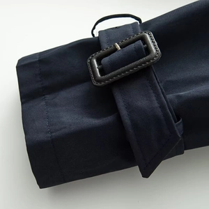 Detail of navy blue trench coat cuff with adjustable strap and textured buckle