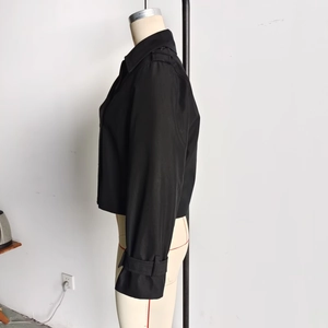 Detail view of black cropped trench jacket showing epaulettes and cuff adjusters on mannequin