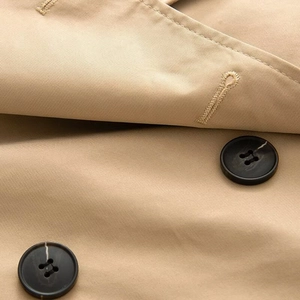 Detail of khaki twill fabric and dark marble buttons on a short double-breasted trench coat