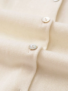 Detailed view of cream knit fabric texture and pearlescent buttons on a polo cardigan