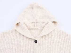 Detail of creamy knit hoodie with coarse texture and contrasting black button closure