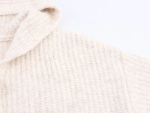 Close-up detail of soft beige chunky knit fabric on a hooded cardigan sweater
