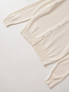 Detailed view of cream knit cardigan featuring ribbed hem and matching round buttons