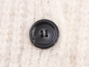Macro shot of black four-hole button on cream chunky knit cardigan sweater fabric