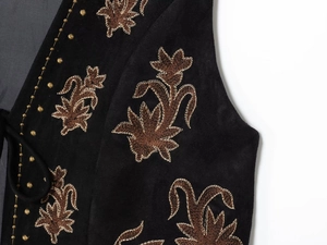 Gros plan de la broderie florale marron et points dorés sur gilet en suédine noire