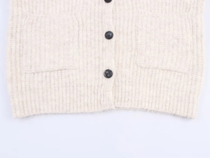 Detail of off-white knit cardigan showing black buttons, wool texture and ribbed hemline