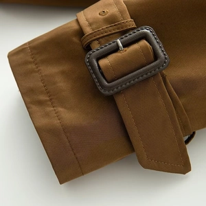 Detail of adjustable cuff strap with matte rectangular buckle on tobacco brown trench coat