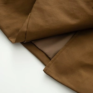 Detailed close-up of brown trench coat fabric featuring fine stitching and smooth lining