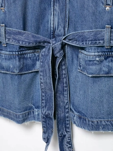 Close-up of blue denim jacket showing waist belt, flap pockets and raw frayed hem