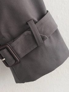 Close-up of adjustable cuff with brown buckle on dark grey cotton trench coat