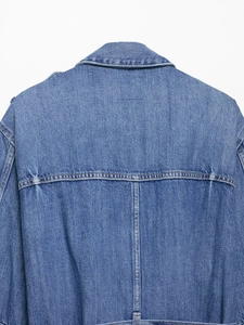 Macro detail of mid-blue denim jacket back featuring twill texture and contrast stitching