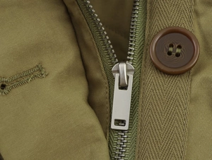 Detailed close-up of heavy-duty metal zipper and resin button on a parka jacket