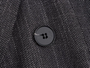 Close-up of black and white tweed texture with a round four-hole button on the blazer