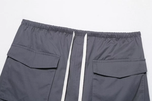 Detail of dark grey cargo shorts with elastic waist, white drawstrings and large flap pockets