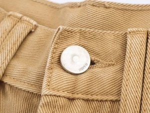 Macro detail of khaki denim waist with silver embossed metal button and twill fabric texture