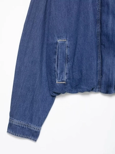 Detail view of deep blue denim jacket showing orange stitching and front pocket texture