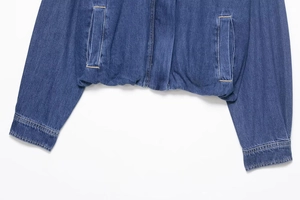 Detail of blue denim jacket with elastic waistband, side pockets and neat stitching