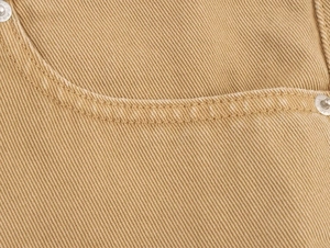 Macro shot of khaki twill fabric showing double stitching and metal rivets on denim jeans