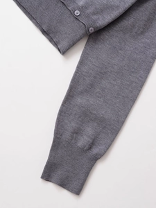 Detail of grey knit cardigan featuring decorative buttons and ribbed cuff texture