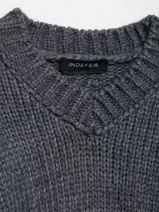 Detailed close-up of a dark grey chunky knit sweater neckline with a brand label