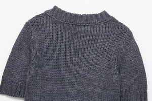Detail view of V-neck neckline and heavy knit texture on dark grey knitted sweater