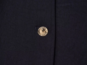 Détail du tissu sergé bleu marine avec un bouton doré texturé sur une veste de blazer