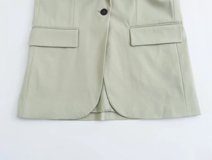 Détail de blazer vert sauge montrant les poches, le tissu lisse et un seul bouton