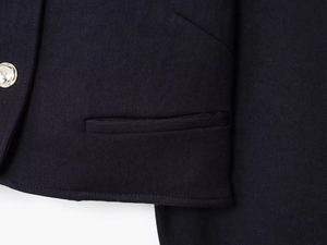 Détail de la poche du blazer bleu marine avec bouton doré perlé et tissu sergé de luxe