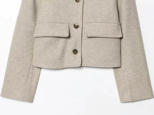 Detail of tweed jacket showing beige wool fabric, pocket flap, and tortoise buttons