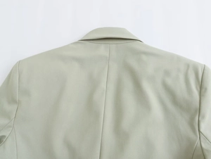 Détail du col et des coutures d'épaule d'un blazer vert sauge sur un fond blanc neutre