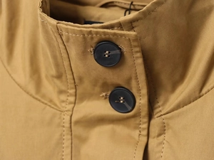 Dettaglio del colletto di un trench khaki con bottoni testurizzati e cuciture fini