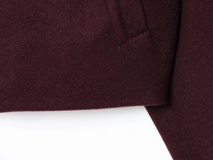 Macro detail of the dark red wool jacket hem and seamless pocket stitching texture