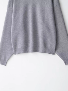 Detail shot of the ribbed hem and cuffs on a grey knit sweater featuring a soft texture