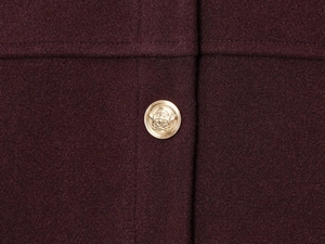 Macro shot of gold embossed button and premium burgundy wool fabric on pilot jacket