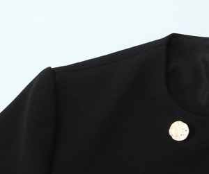 Dettaglio del colletto di un blazer nero con bottone dorato a effetto martellato