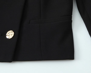Dettaglio del blazer corto nero con bottone metallico dorato e tasca a filetto elegante