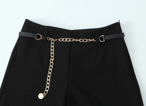 Dettaglio dei pantaloni neri a vita alta con elegante catena in metallo dorato e cintura