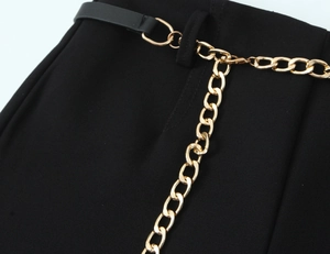 Dettaglio dei pantaloni neri con cintura in pelle e una vistosa catena dorata