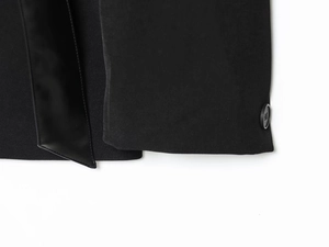 Detail view of black blazer sleeve featuring leather trim and a single round button