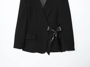 Detail of black blazer featuring a large faux-leather bow belt and flap pockets