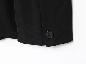 Macro detail of black wrap blazer sleeve featuring textured twill fabric and round button