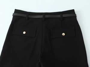 Dettaglio vita dei pantaloni neri con cintura coordinata e bottoni dorati decorativi