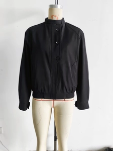 Detail of black jacket with stand collar, front buttons and elasticated cuffs and hem