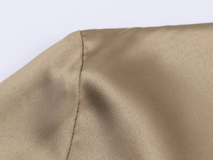 Close-up of golden bronze satin fabric texture and neat shoulder stitching on a long-sleeved shirt