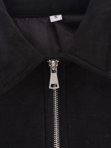 Detail von Metallreißverschluss und Kragen einer schwarzen Wildlederjacke mit S-Etikett