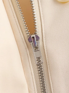 Detailed close-up of premium metal zipper and textured beige fabric on a women jacket
