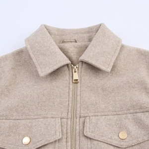 Detail of beige wool jacket showing gold metal zipper and textured fabric finish