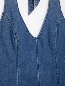 Detail of blue denim halter neck dress featuring deep V-neck and visible topstitching